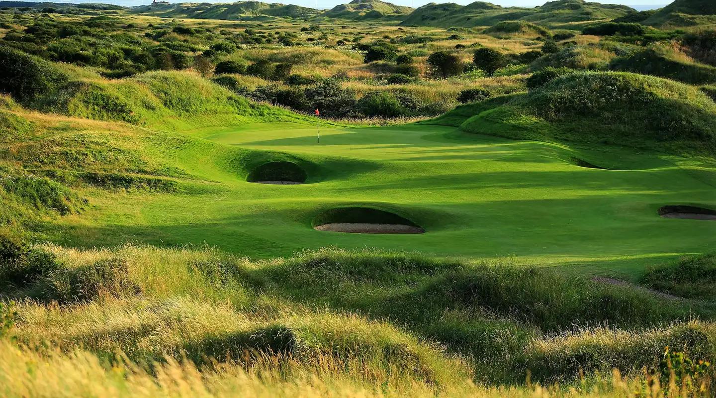 A lush green nestled between rolling dunes with challenging bunkers.