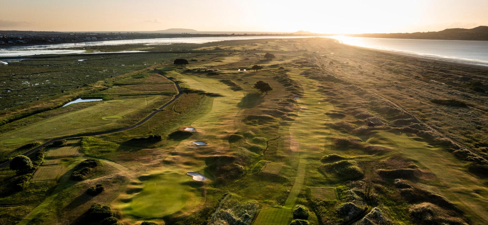 A dramatic sunset over a coastal golf course with winding fairways and natural dunes.