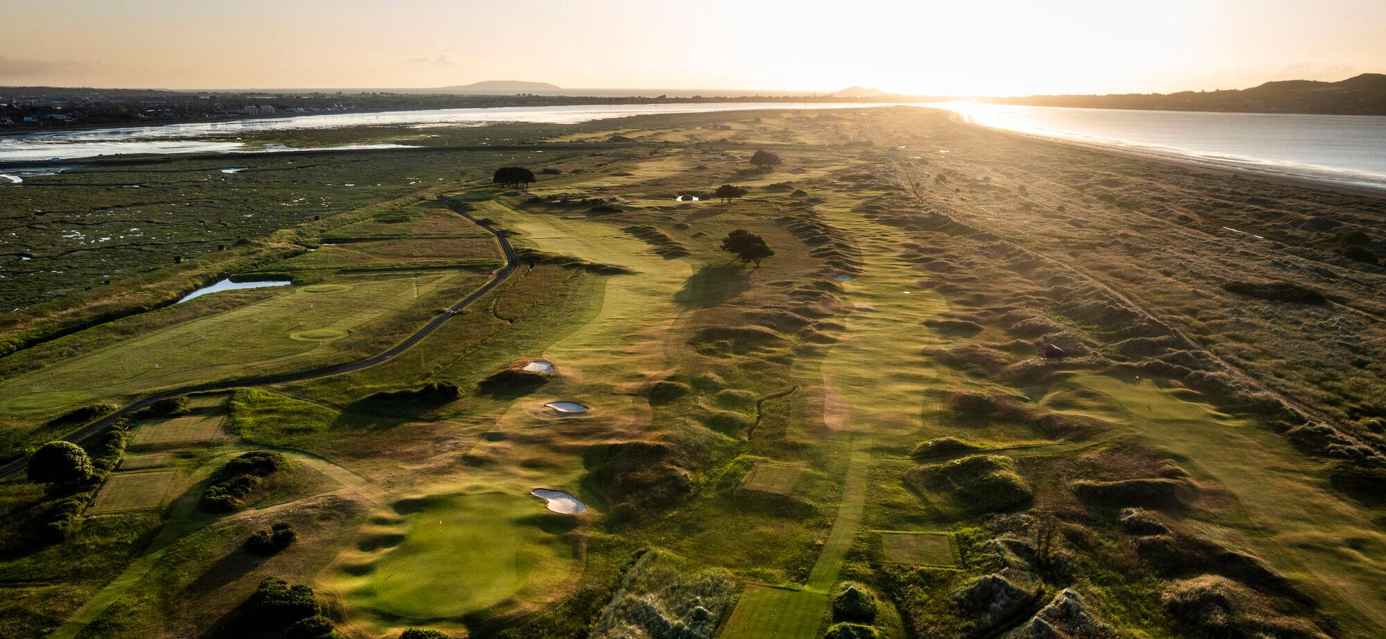 A dramatic sunset over a coastal golf course with winding fairways and natural dunes.