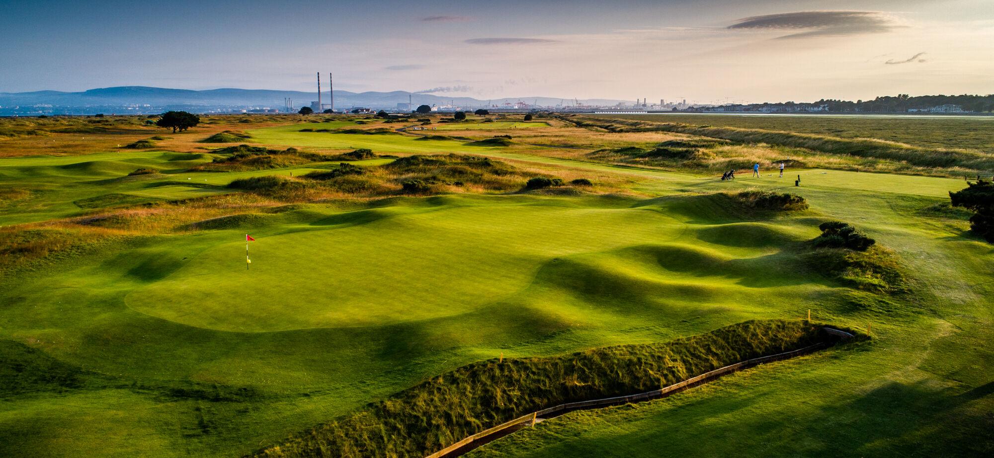 A wide view of a beautifully contoured golf green with players enjoying a game.
