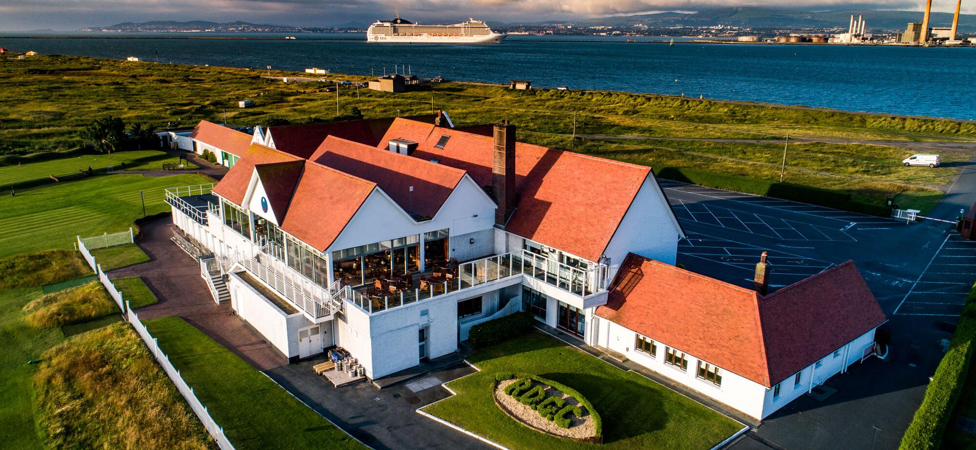 A clubhouse with red roofs overlooking the water and surrounded by open greens.