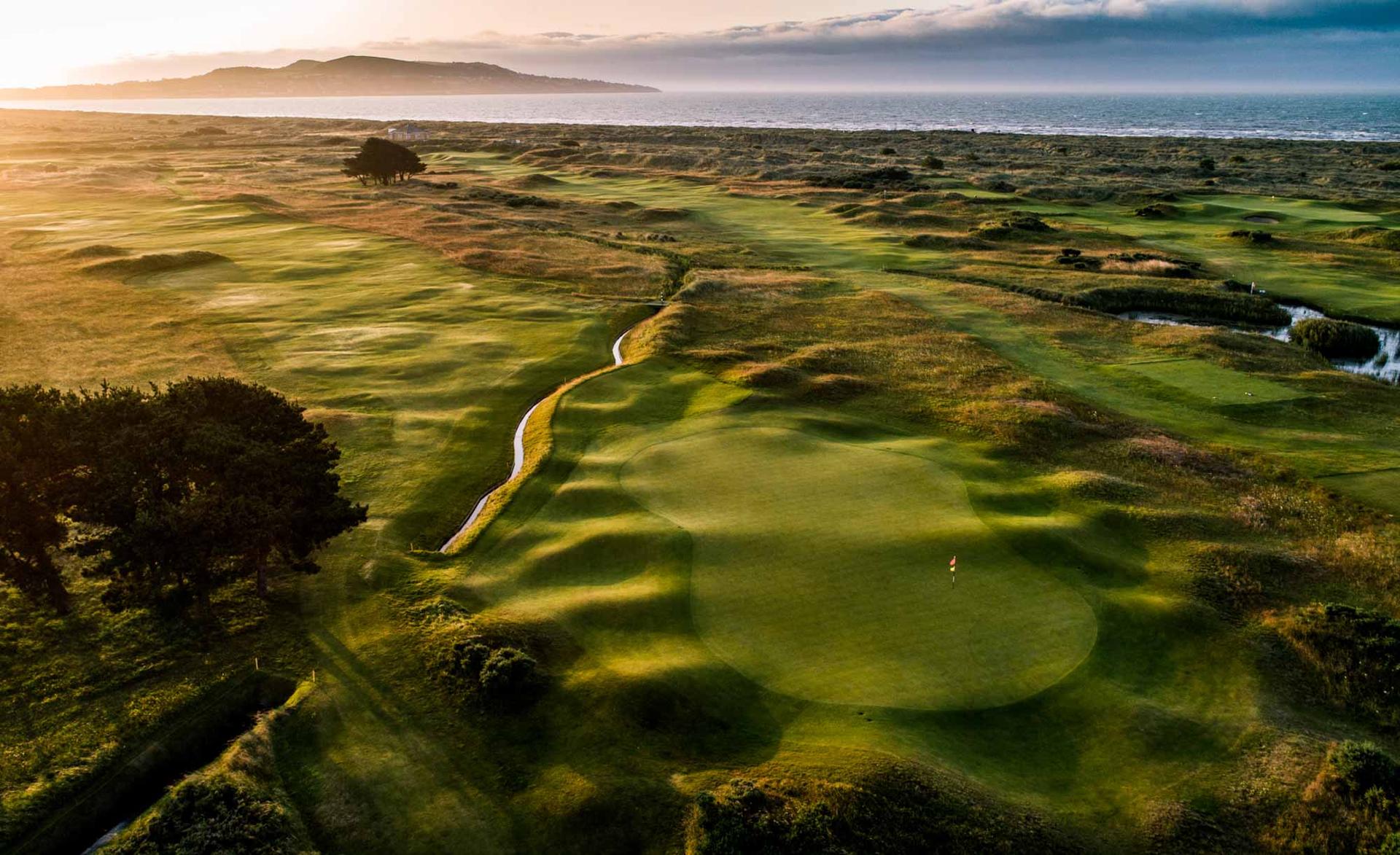 A stunning golf course at sunset, with rolling greens and the ocean in the distance.