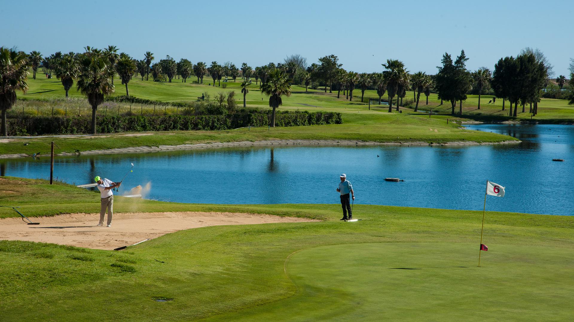 Player playing out of a bunker onto the green with a water hazard behind