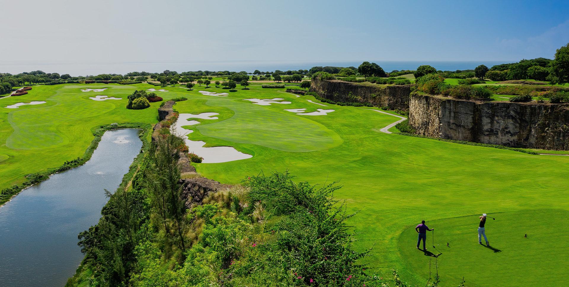 Golfers tee off against the backdrop of rugged cliffs, pristine fairways, and a calm river flowing through the course.