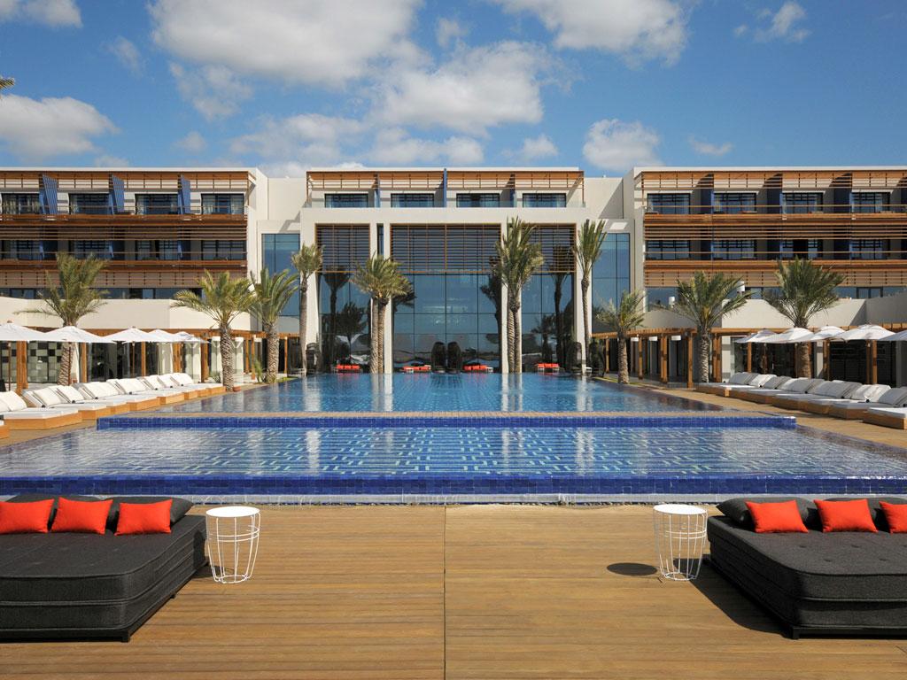 Outdoor swimming pool surrounded by sunbeds and palm trees at the Sofitel Essaouira Mogador Golf & Spa