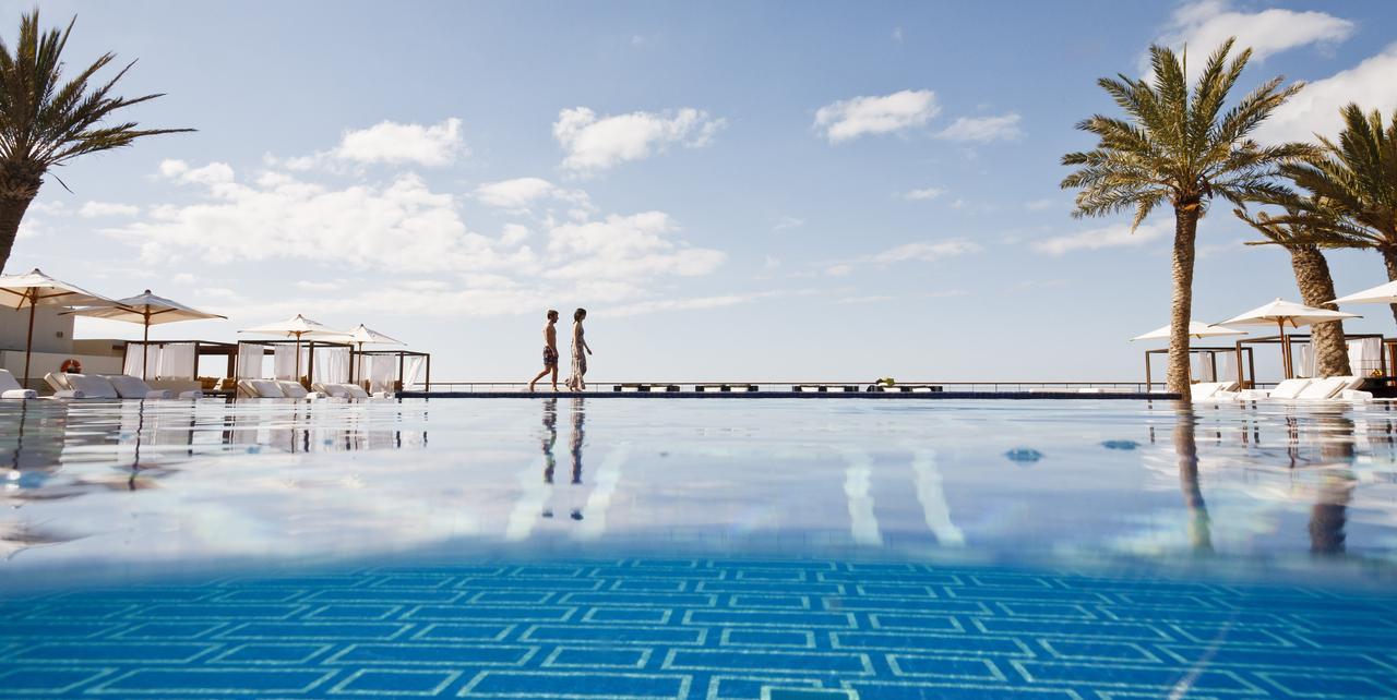 Guests walking along the outdoor swimming pool surrounded by sunbeds