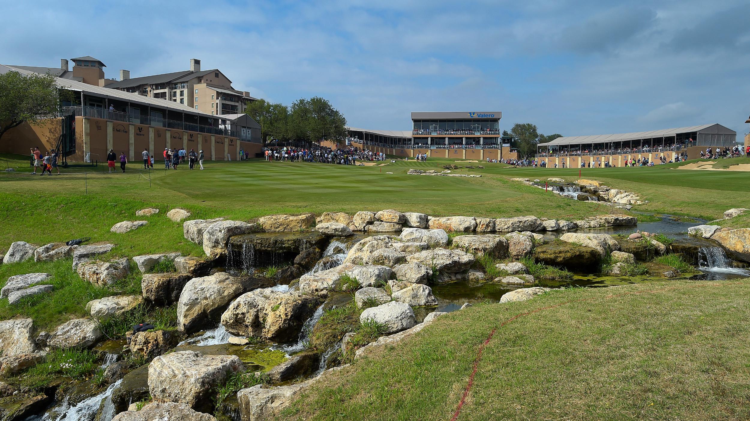 Championship golf course with cascading rock waterfalls and spectator stands during a PGA Tour event.