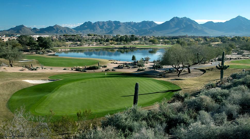 A golf course overlooking a reflective lake with mountains in the background.