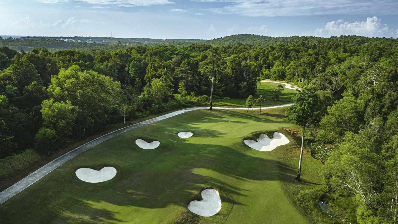 A lush golf course surrounded by dense forest with multiple sand bunkers.