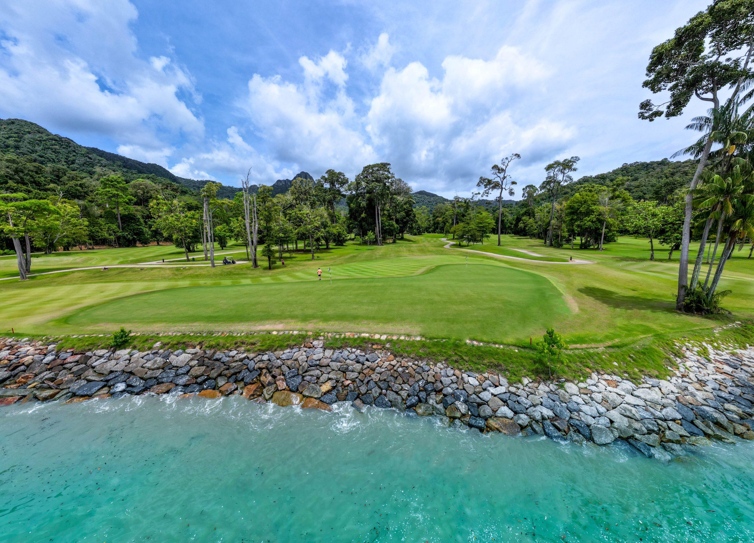 A manicured fairway placed on the coast under cloudy blue skies