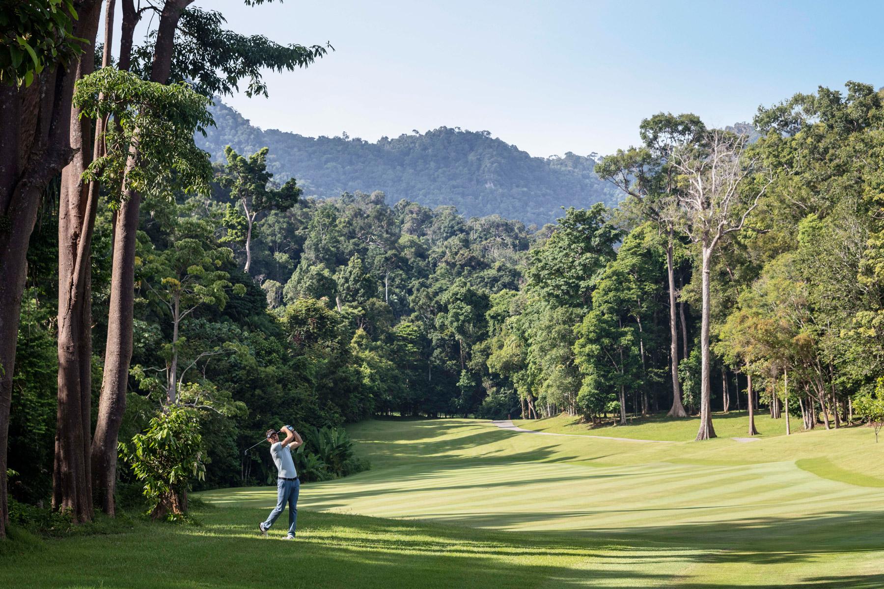 A golfer swinging on a wide fairway surrounded by forest like trees