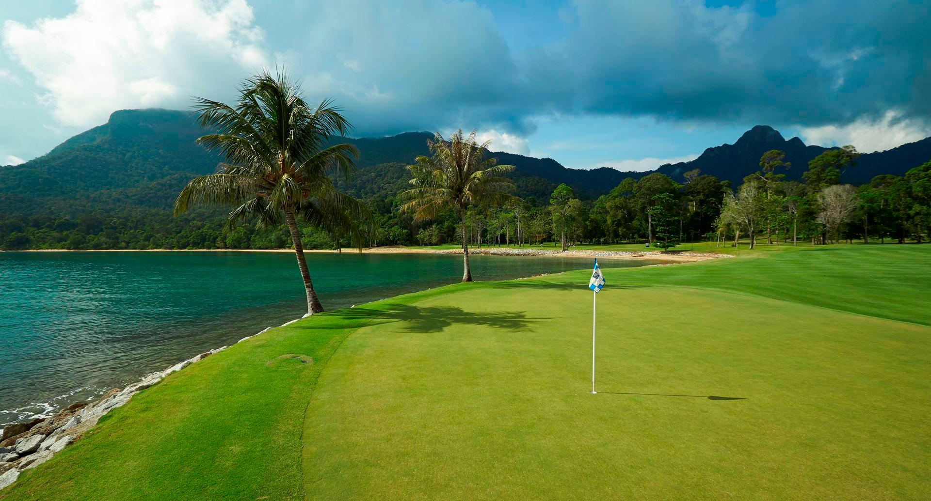 A smooth green placed next to the sea with mountain views in the distance