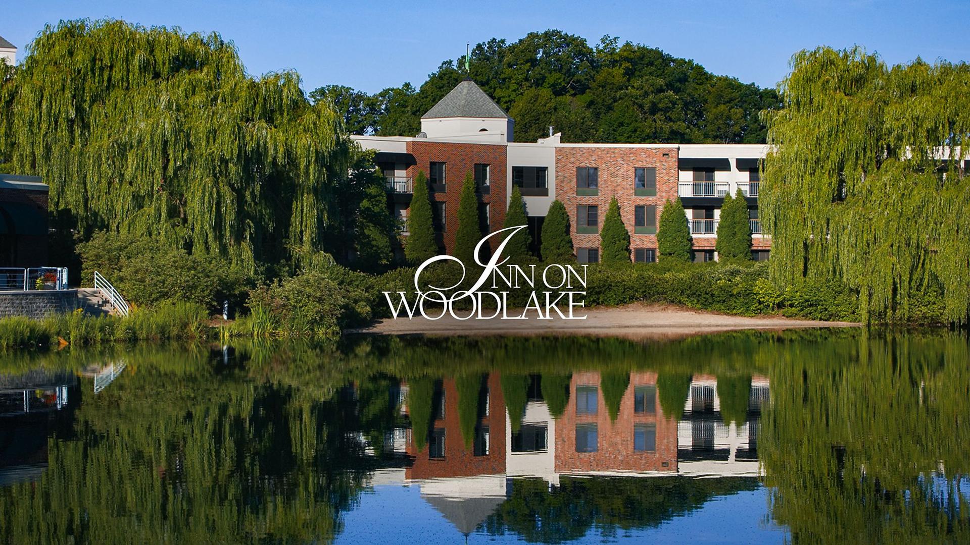 The Inn on Woodlake building reflecting in a serene lake surrounded by trees.