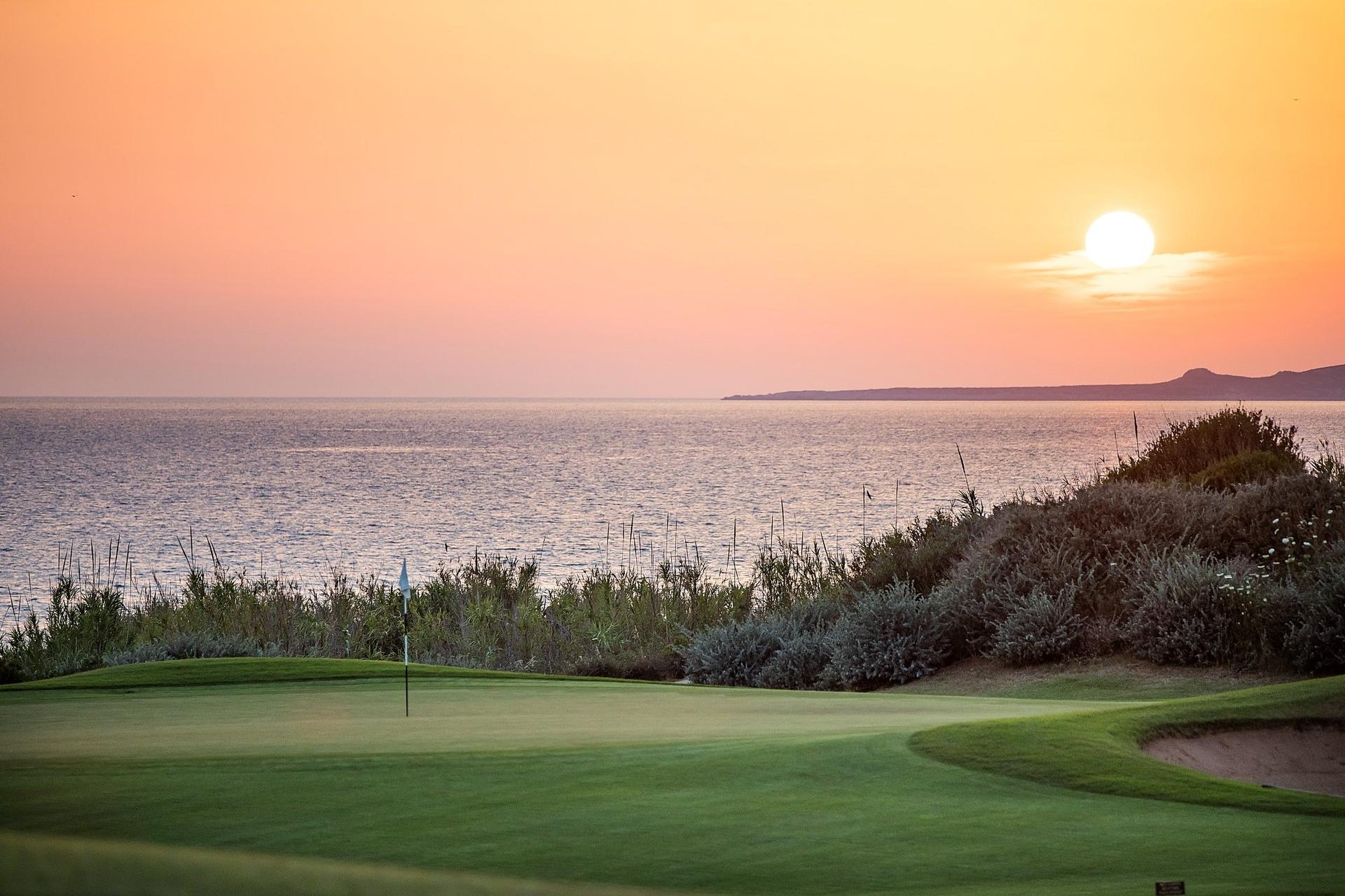 A serene golf green overlooks the ocean at sunset, creating a peaceful coastal view.