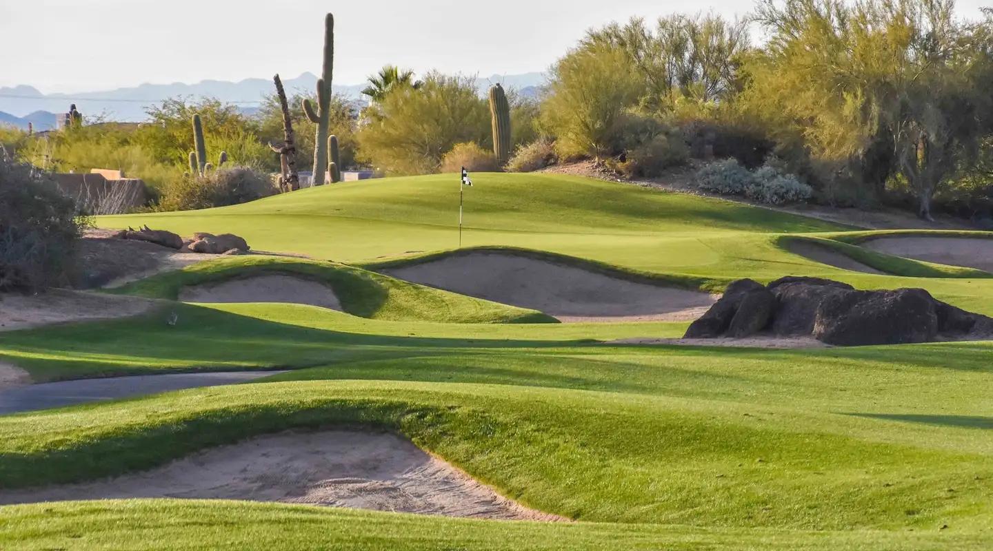 A desert golf course hole surrounded by cacti, rocks, and sand bunkers.