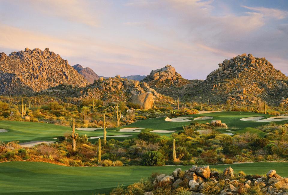 A breathtaking desert golf course with rugged rocky mountains in the background.
