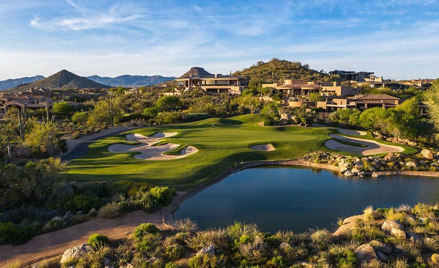 A picturesque green beside a pond with desert homes in the background.