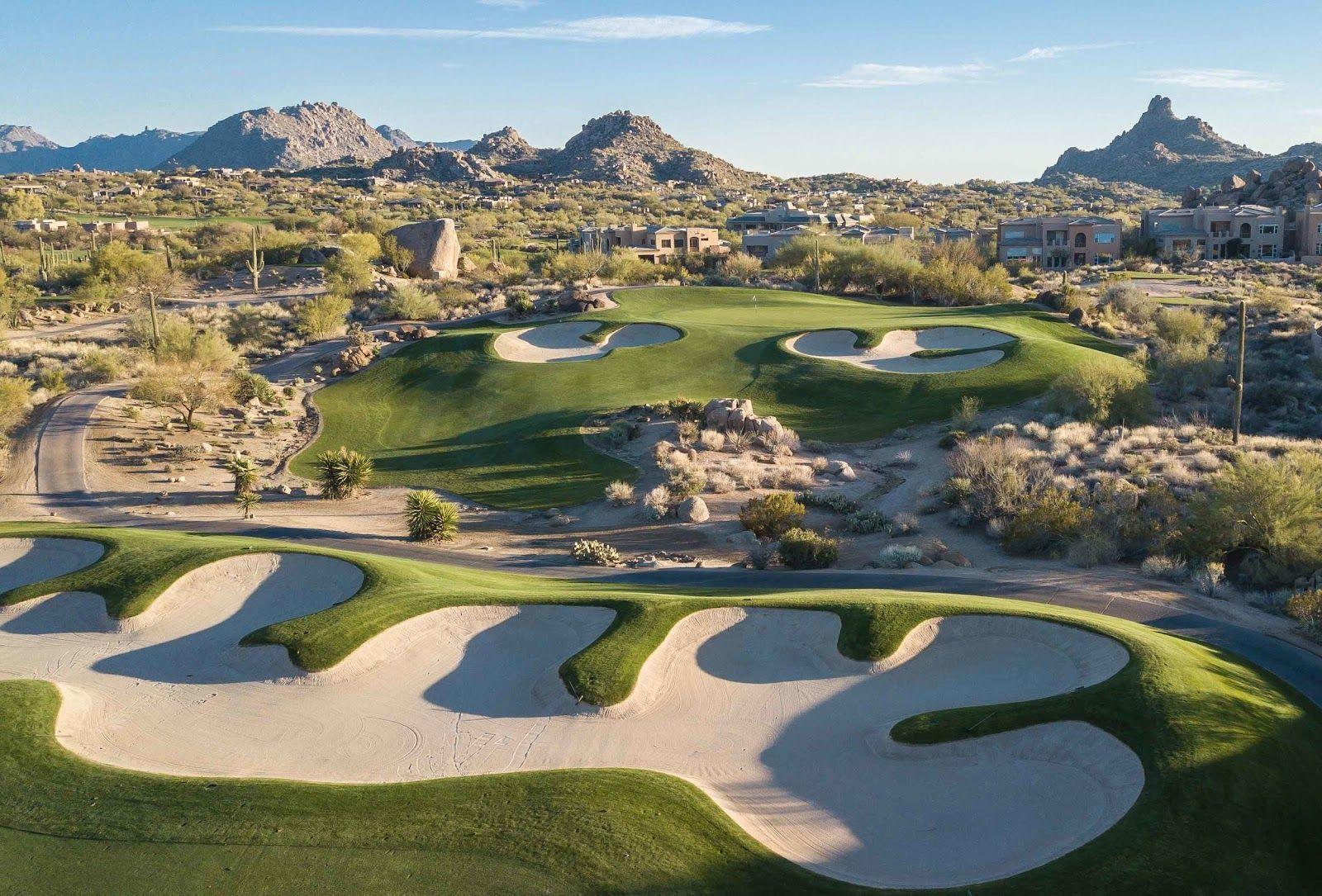 A desert golf course with uniquely shaped sand bunkers and surrounding rocky terrain.