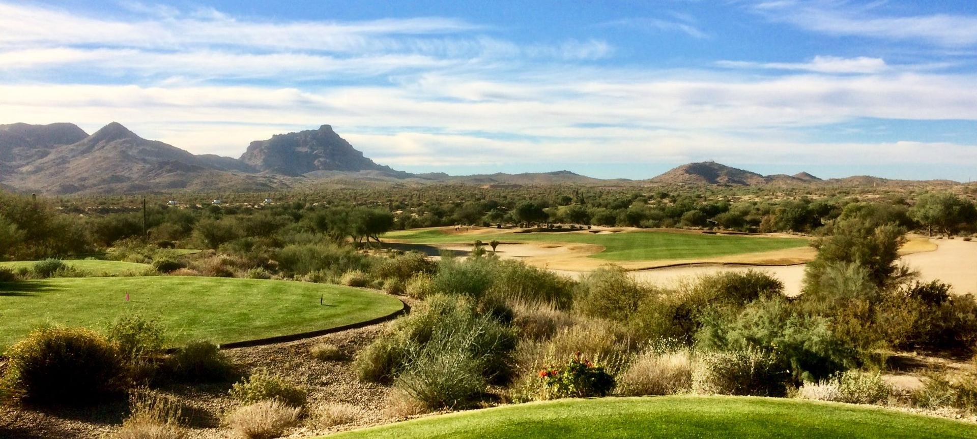 A distant green nestled among desert plants with mountains as the backdrop.
