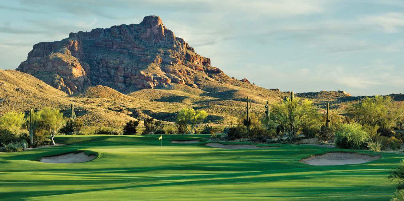 A wide panoramic view of a desert golf course under a pinkish sunset sky.