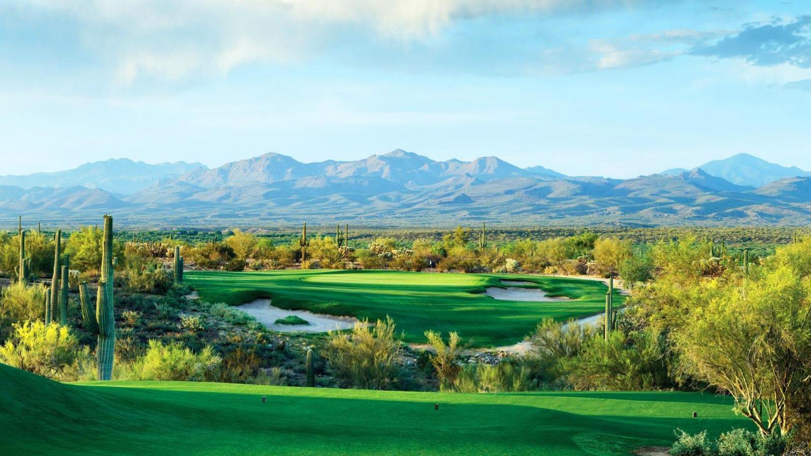 A golf hole set against a backdrop of sprawling mountains and desert terrain.