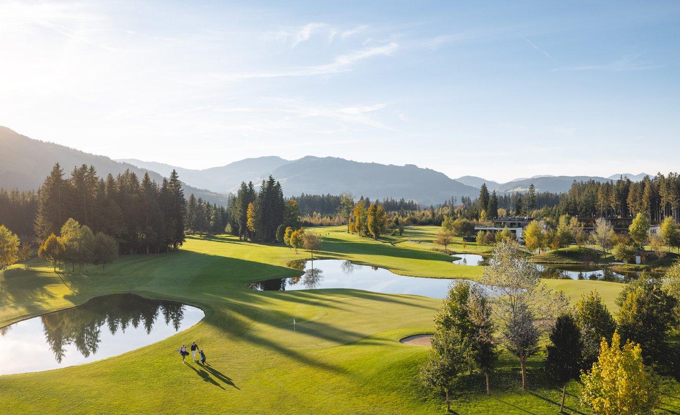 Golfers walking near calm ponds on a lush green course.