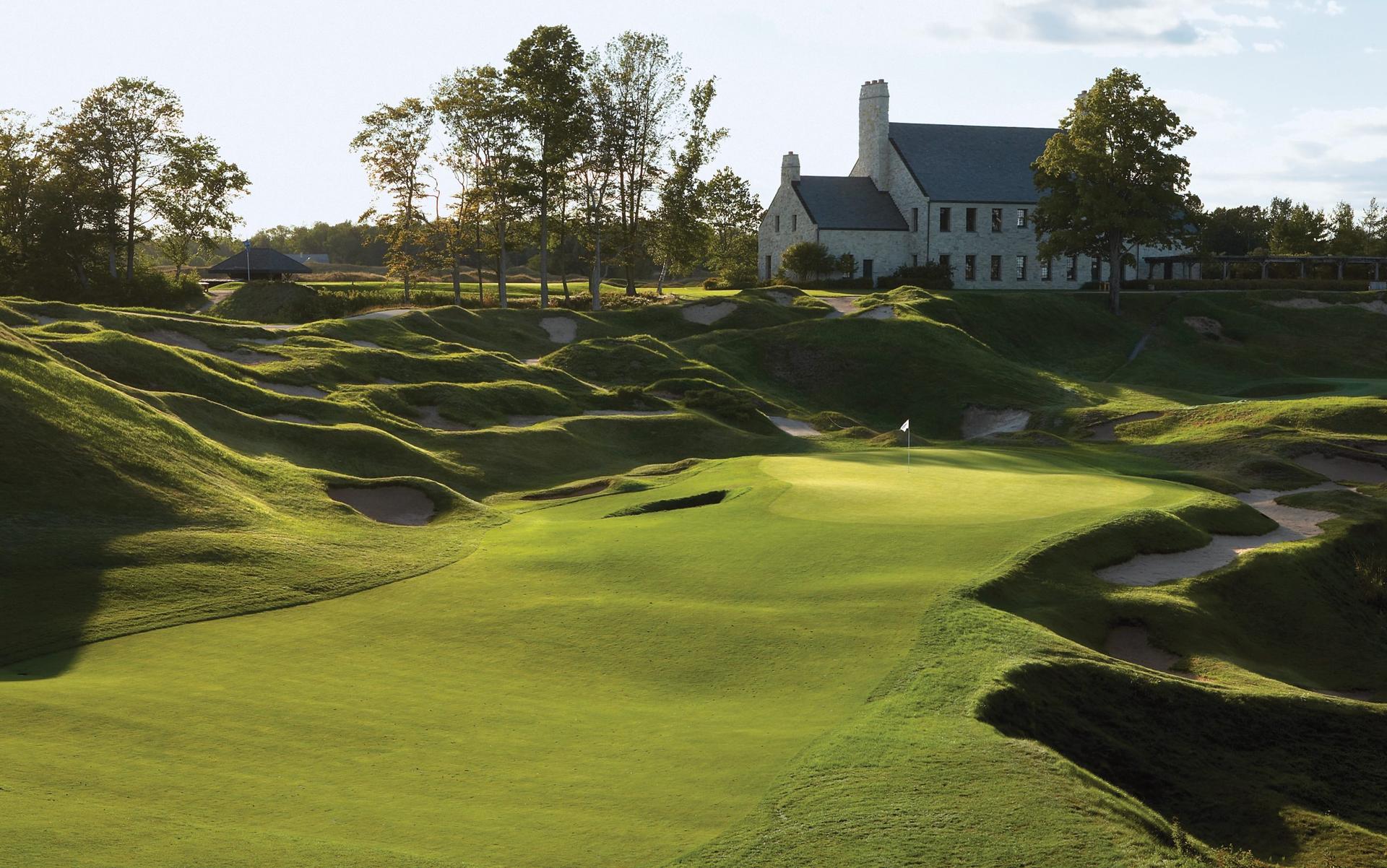 Rolling dunes with sand bunkers surrounding a smooth green with the clubhouse in the back
