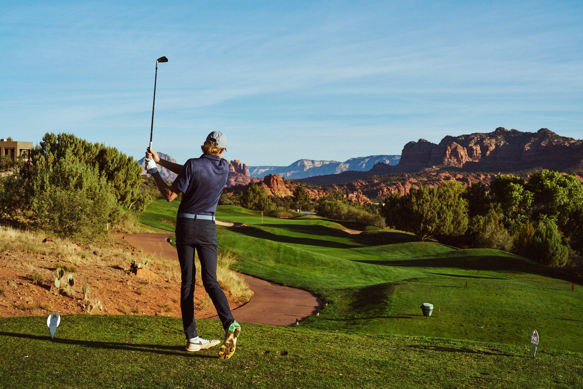 Golfer hitting a shot on a well maintained fairway towards rolling dunes and a smooth green with mountain views
