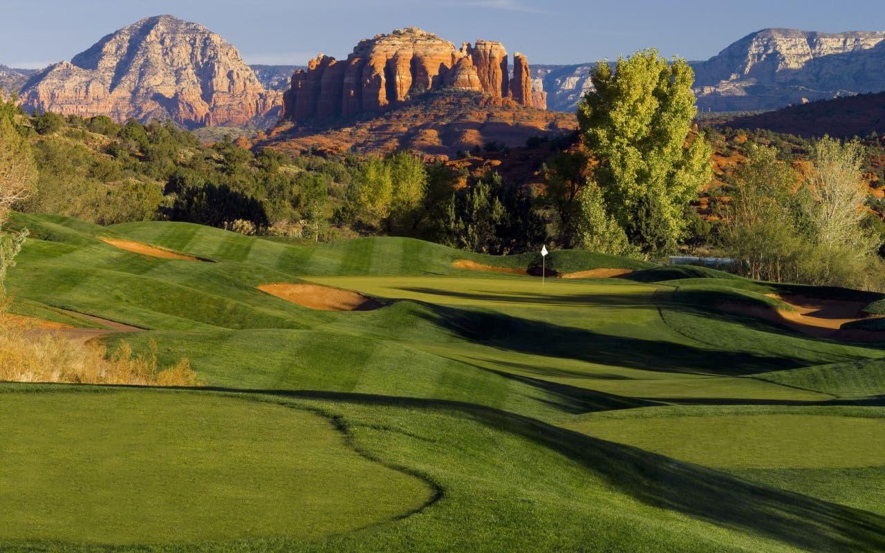 Rolling dunes surrounding a smooth green littered with sand bunkers and mountain views in the distance