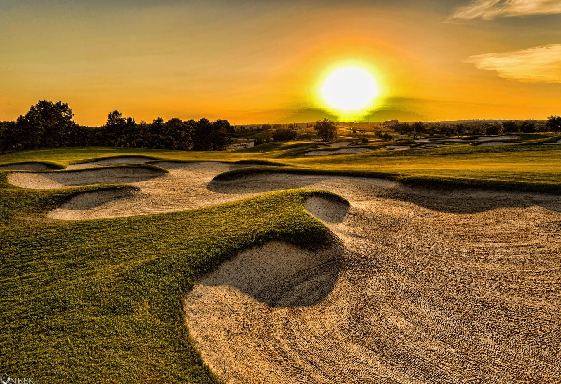 Sun setting over a large sand bunker surrounded by a well maintained fairway