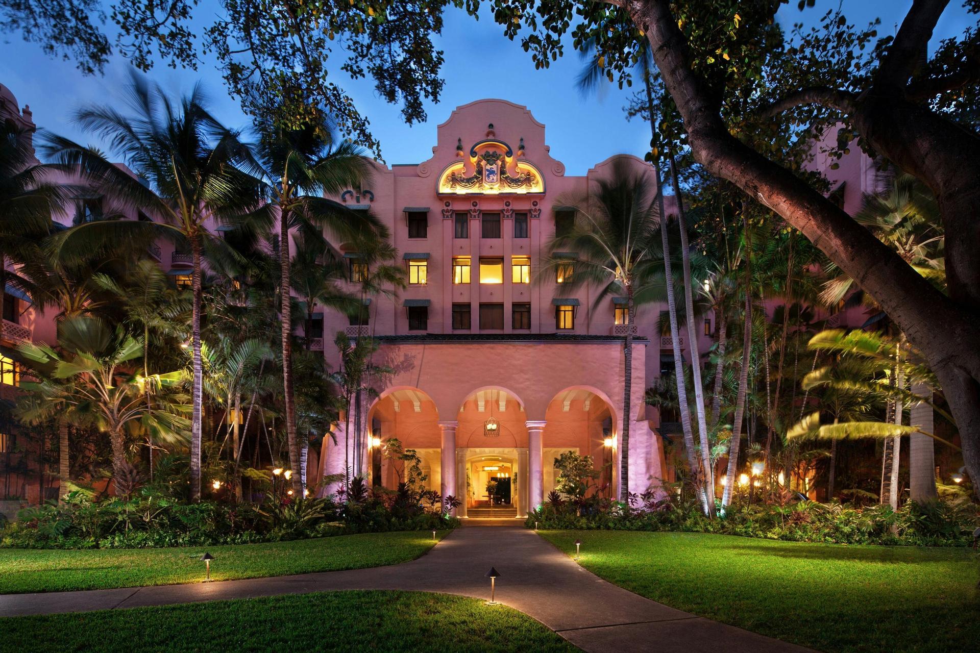Exterior view of the hotel building being lit up at evening surrounded by jungle trees