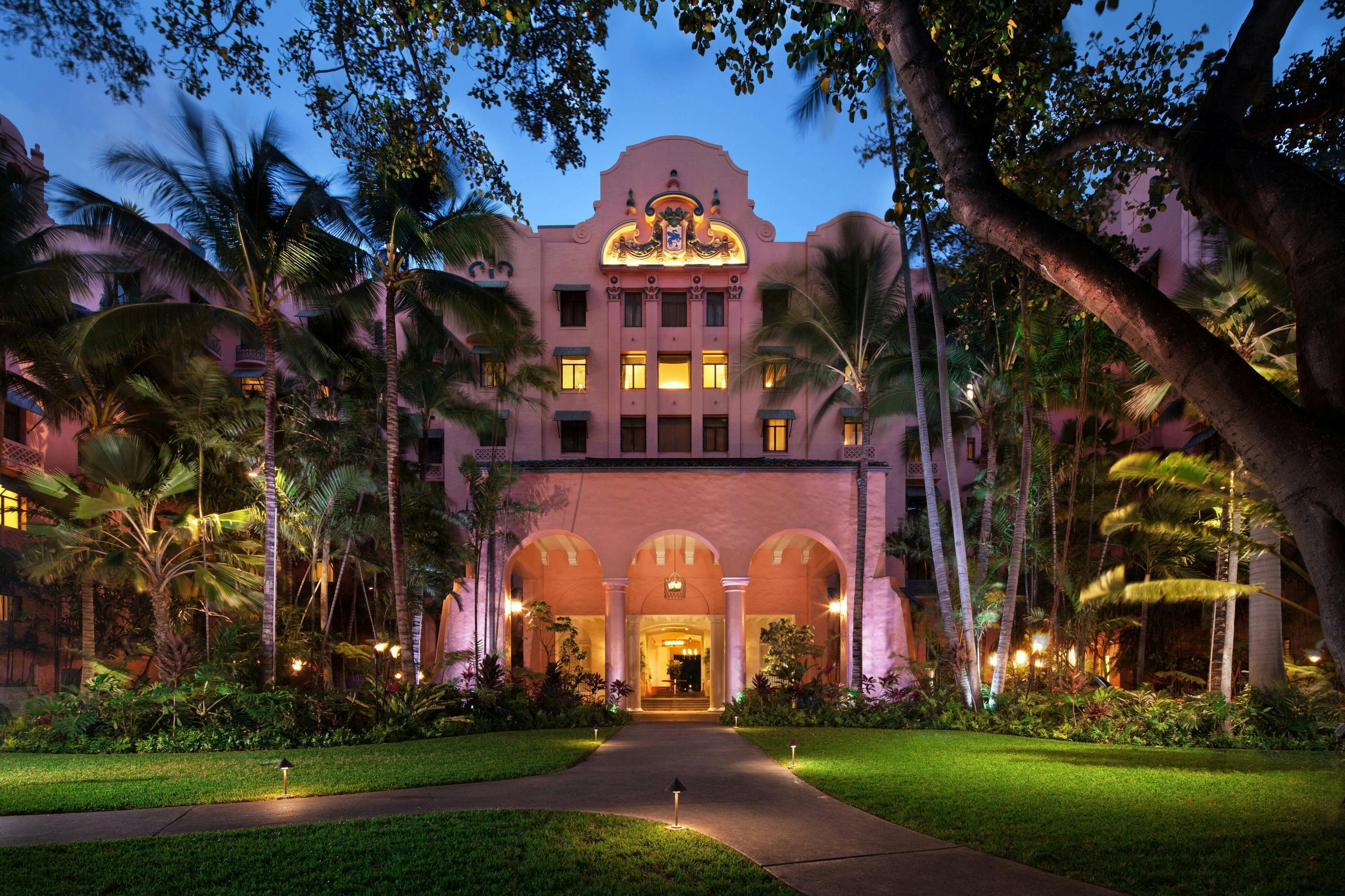Exterior view of the hotel building being lit up at evening surrounded by jungle trees