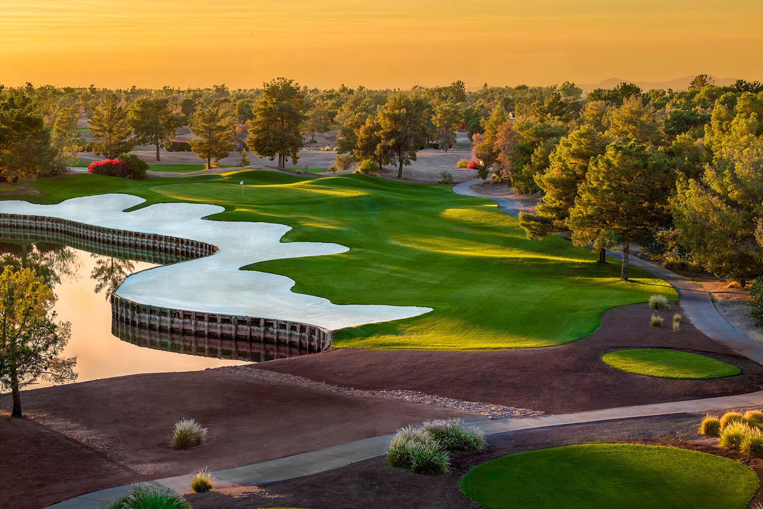 Sun setting over a well maintained fairway next to a sand bunker and water hazard